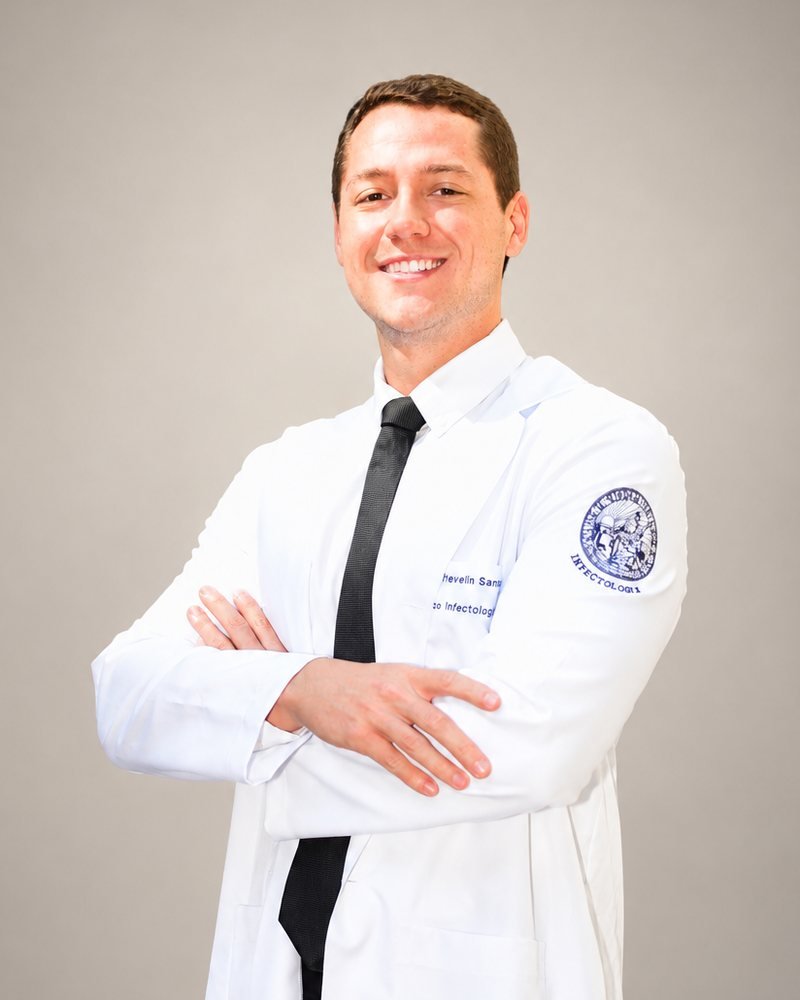 Dr. Caio Trevelin Sambo de jaleco, sorrindo, com os braços cruzados